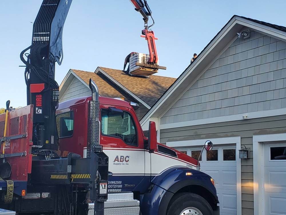 Crane truck lifting roofing materials onto home.